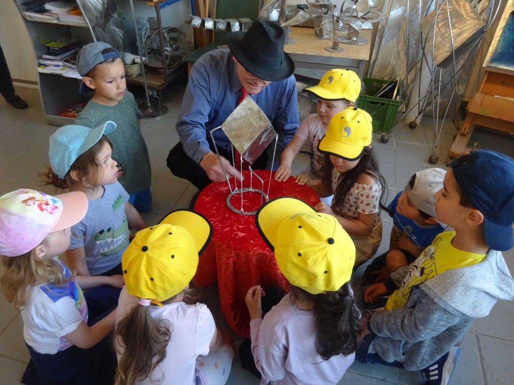 Kinder stehen im Kreis mit einem Metallbildhauer und dessen Kunstwerk