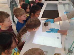 Mitarbeiterin des Badischen Landesmuseums zeigt einer Gruppe von Kindern ein jahrtausende altes Relikt.