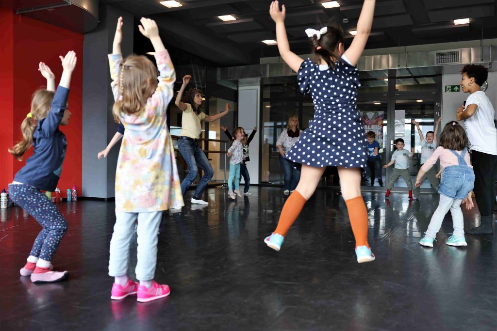 Im Kreis stehende springende Kinder und Erwachsene im Tanzraum