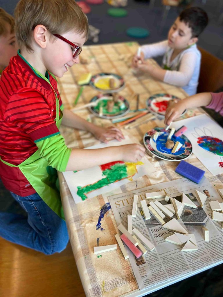 Eine Gruppe von Kindern sitzt an einem Tisch und kreieren mit Stempeln Bilder.