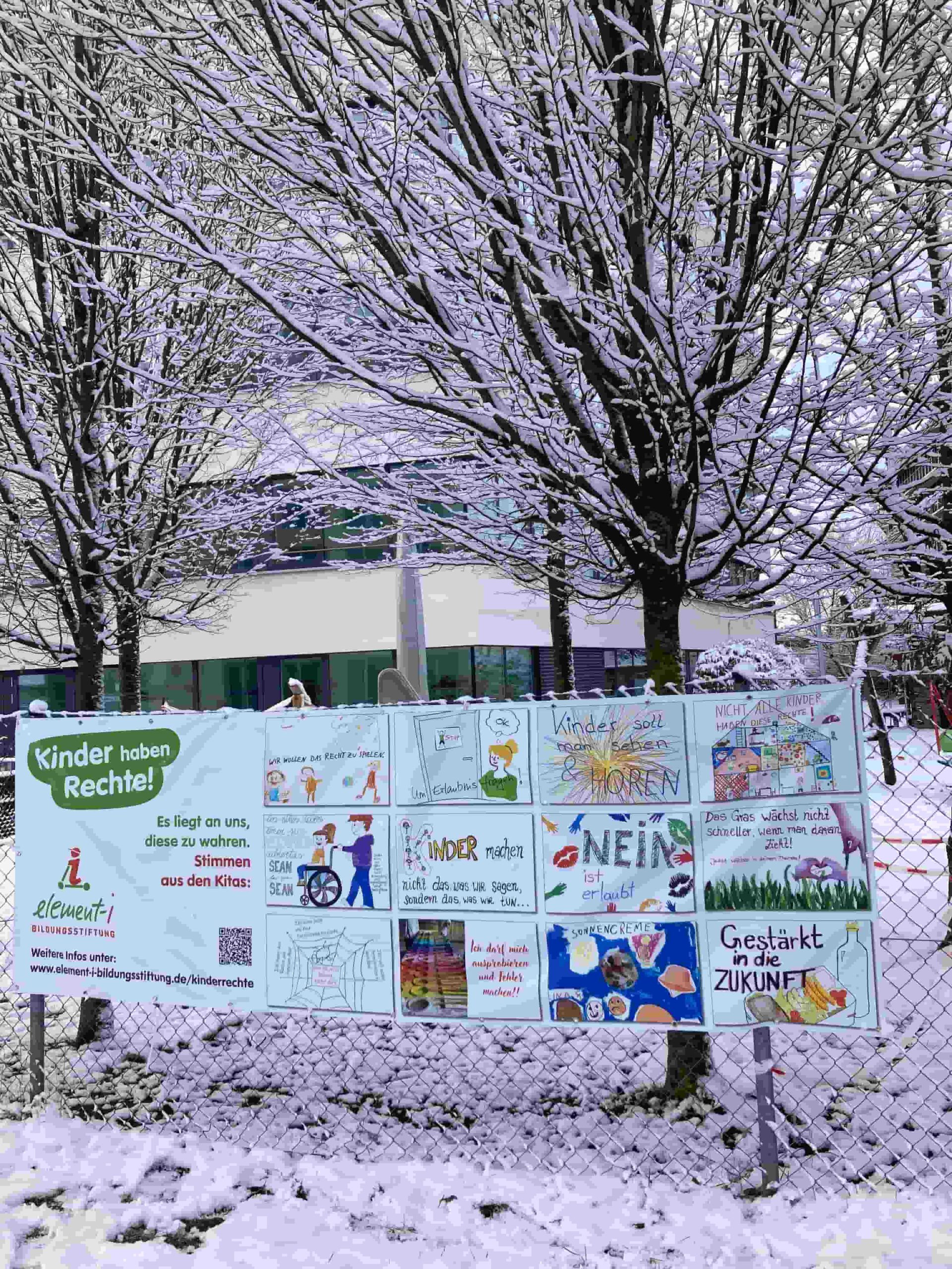 Kinderrechte-Banner an Gartenzaun umgeben von Bäumen und Schnee.